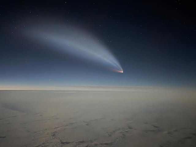 A Vandenberg rocket launch plume lit against a dark blue sky above the clouds at dusk